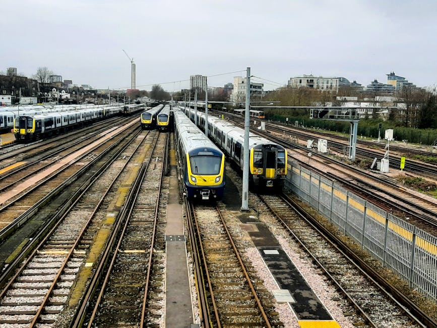 An extensive railway yard with multiple sets of parallel train tracks, some of which are occupied by modern yellow and gray commuter trains. The trains are parked closely together, with the closest tw